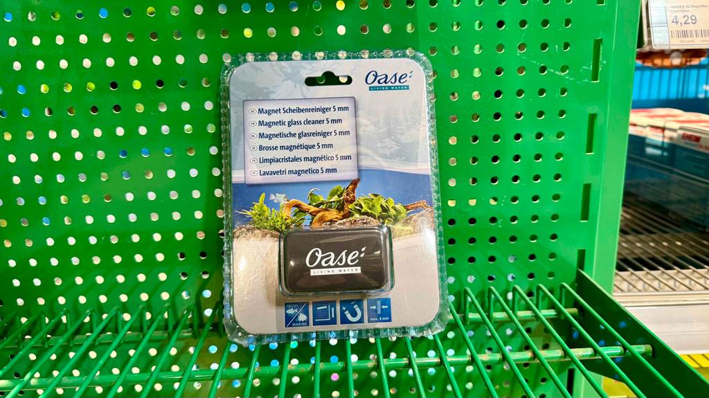 Ein verpackter Aquarium-Scheibenreiniger seht zum testen in einem grünen Lochregal.