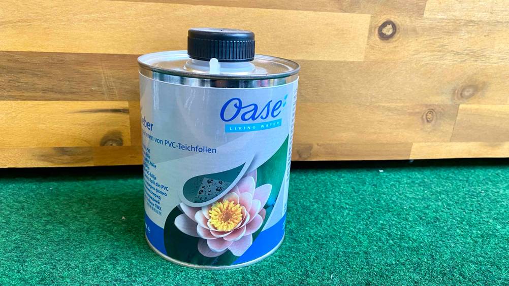 Im Test: Eine Dose Teichfolienkleber auf einem Kunstrasen vor einer Holzfläche.