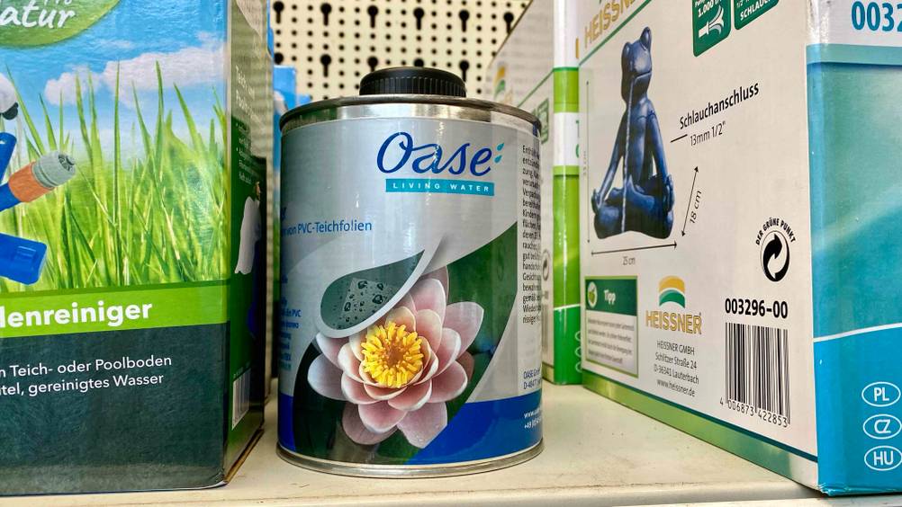 Ein Kanister getesteter Teichfolienkleber steht neben anderen Produkten in einem Verkaufsregal.