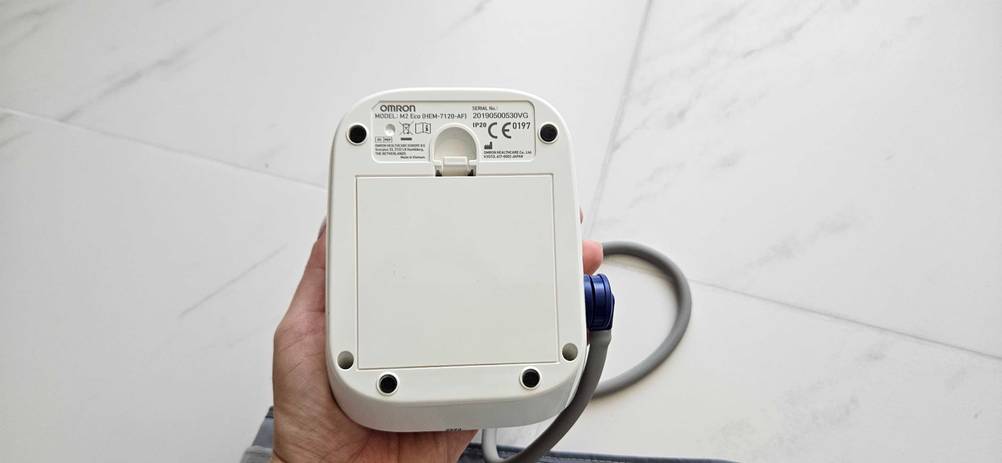 Oberarm-Blutdruckmessgerät getestet: Eine Hand hält die Rückseite des Gerätes mit der Batteriekappe nach oben.