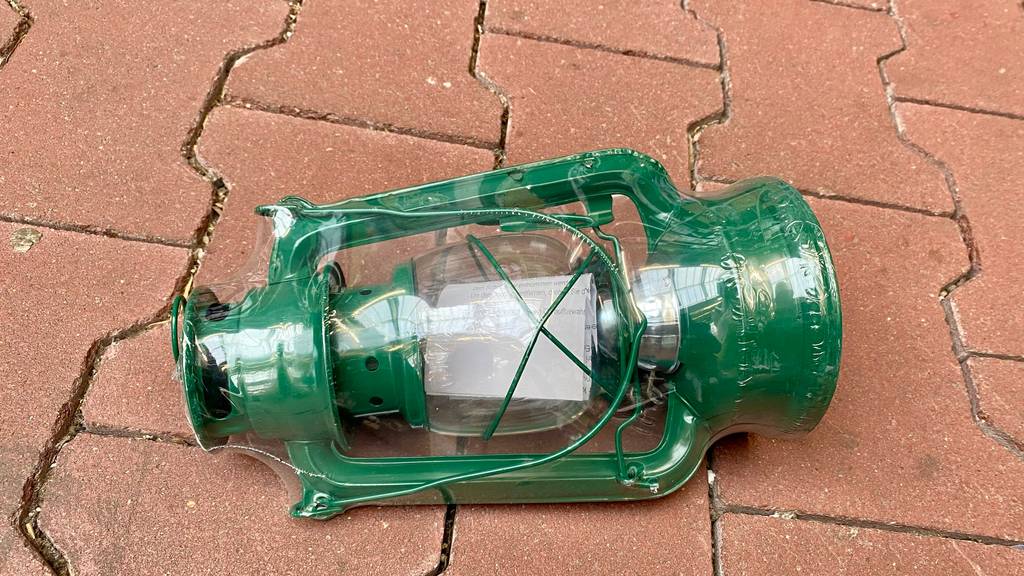 Eine grüne, in Zellophan verpackte Petroleumlampe liegt zum Test bereit auf dem Boden.