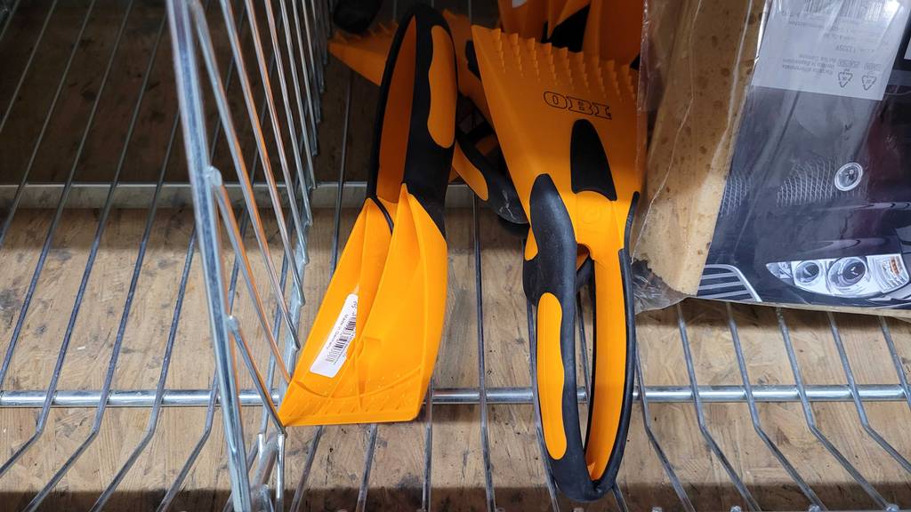 Mehrere orange-schwarze Eiskratzer im Test liegen in einem Verkaufskorb des Baumarktes OBI.