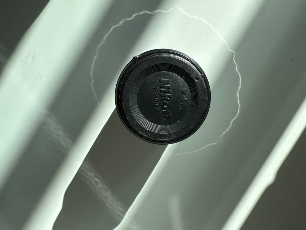 Ein getestetes Objektiv für eine Nikon-Kamera liegt auf einem weißen Tisch. 
