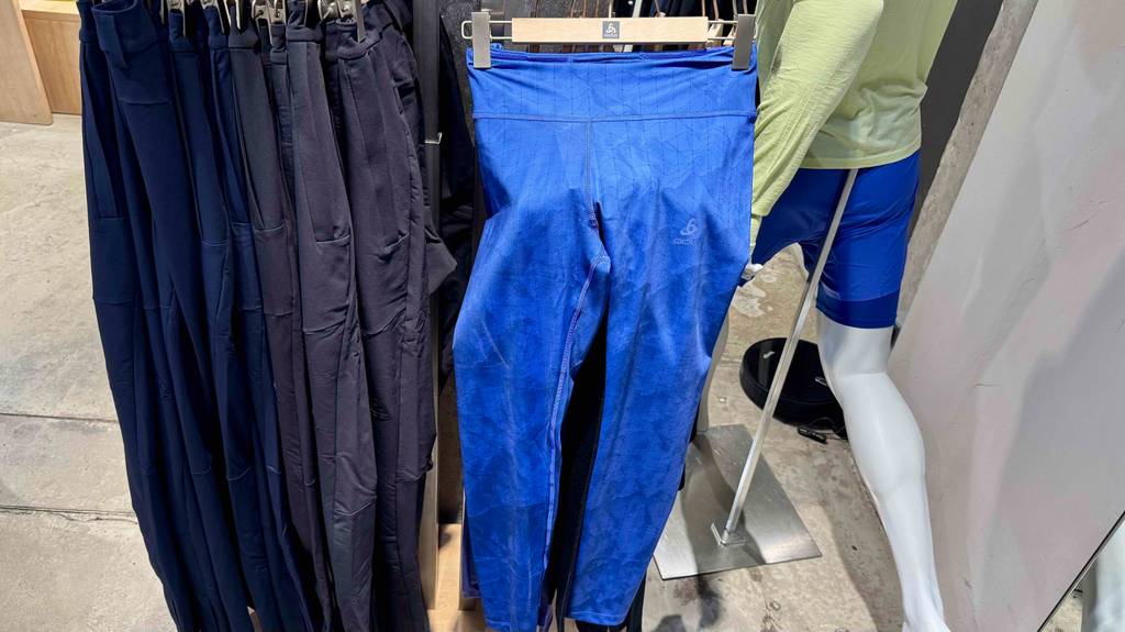Die leuchtend blaue, getestete Damen-Langlaufhose hängt zwischen weiteren verschiedenfarbigen Langlaufhosen und einer Modepuppe an einem Ständer im Geschäft.