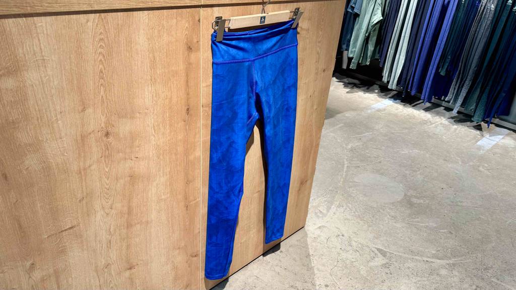 Die Langlaufhose-Damen im Test hängt in voller Länge vor einer Holzwand in einem Verkaufsbereich mit weiteren verschiedenfarbigen Langlaufhosen.