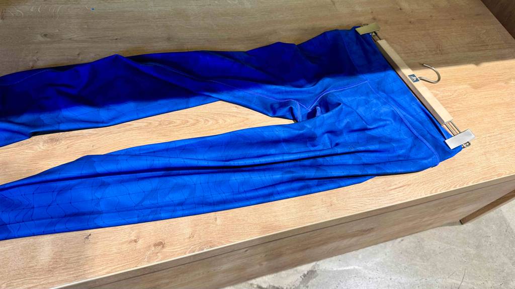 Die getestete Damen-Langlaufhose in leuchtendem Blau liegt inklusive Bügel der Länge nach auf einer Holzoberfläche.