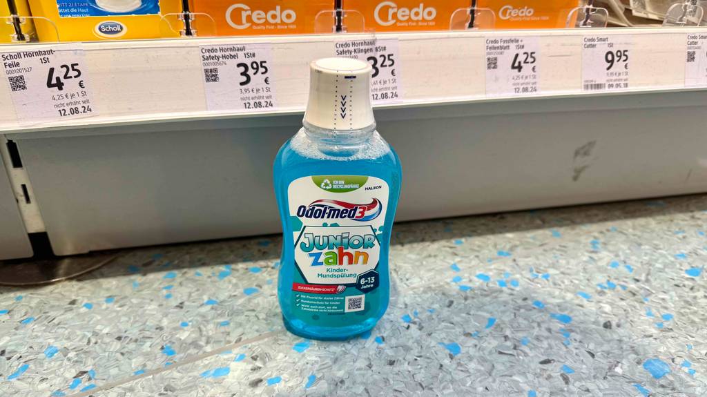 Eine Kunststoffflasche mit Kinder-Mundspülung im Test steht vor einem Verkaufsregal auf dem Boden.