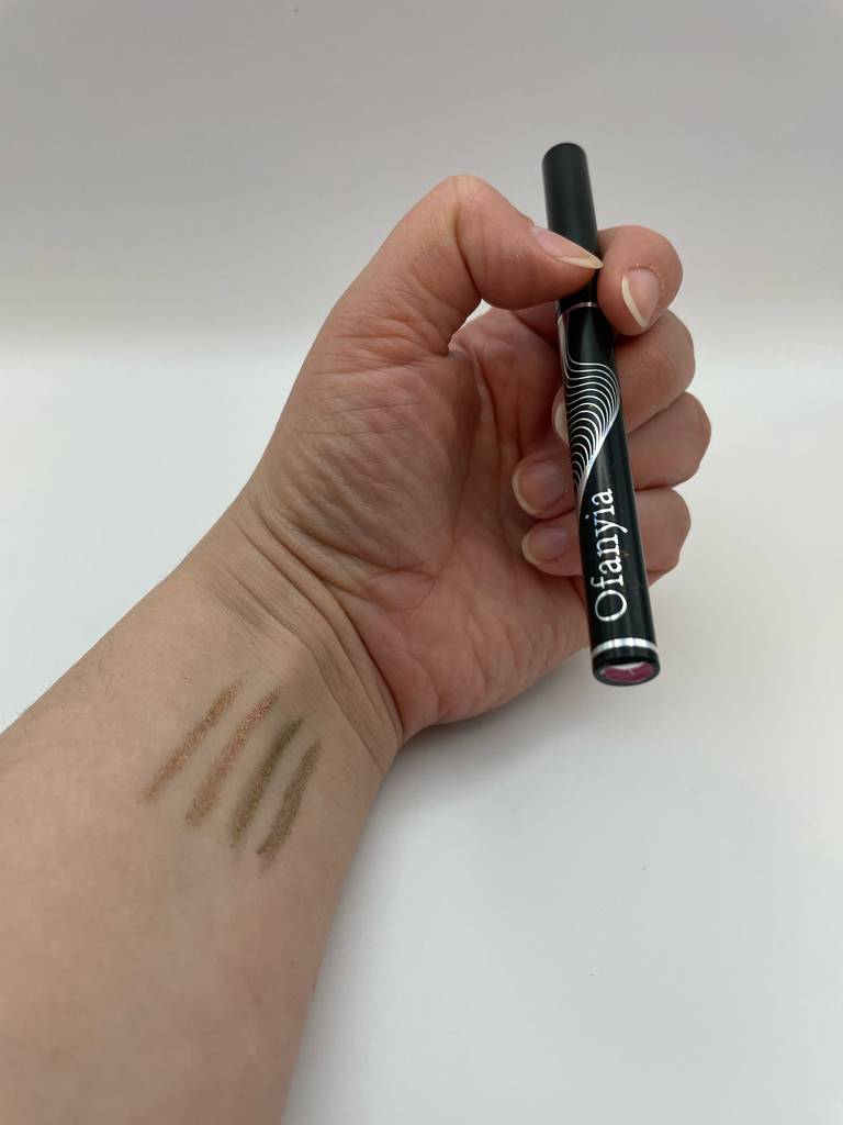 Eine Hand hält einen getesteten Gel-Eyeliner über einer weißen Oberfläche.