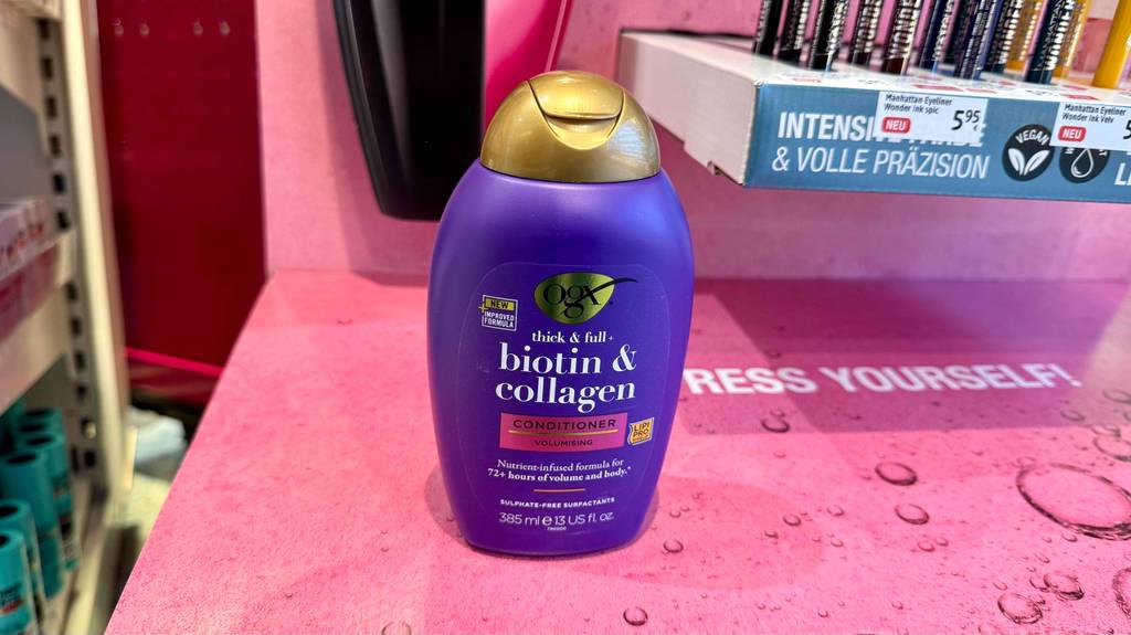 Eine violettfarbene Flasche mit getestetem Collagen-Shampoo steht auf einem pinkfarbenen Karton vor kosmetischen Produkten.