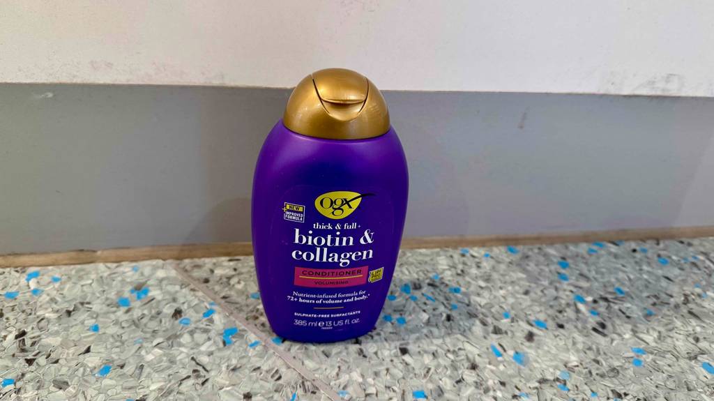 Eine violettfarbene Flasche mit Collagen-Shampoo im Test steht auf einem Linoleum-Boden.