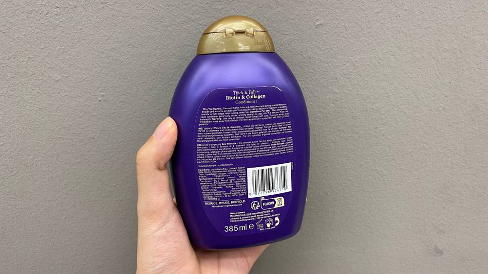 Hand hält eine Flasche getestetes OGX-Shampoo mit der Rückseite nach vorne.