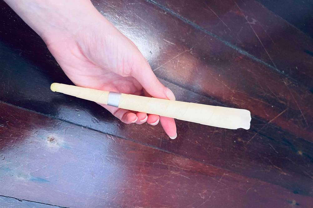 Hand hält eine Ohrenkerze, zum Test bereit, über einer hölzernen Oberfläche.