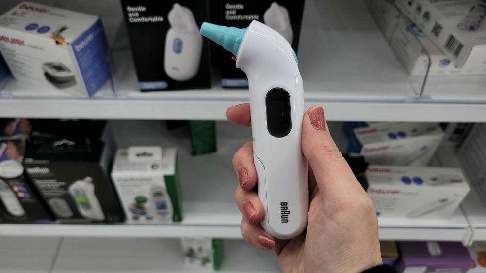 Eine Hand hält ein getestetes Ohrthermometer vor ein Verkaufsregal.