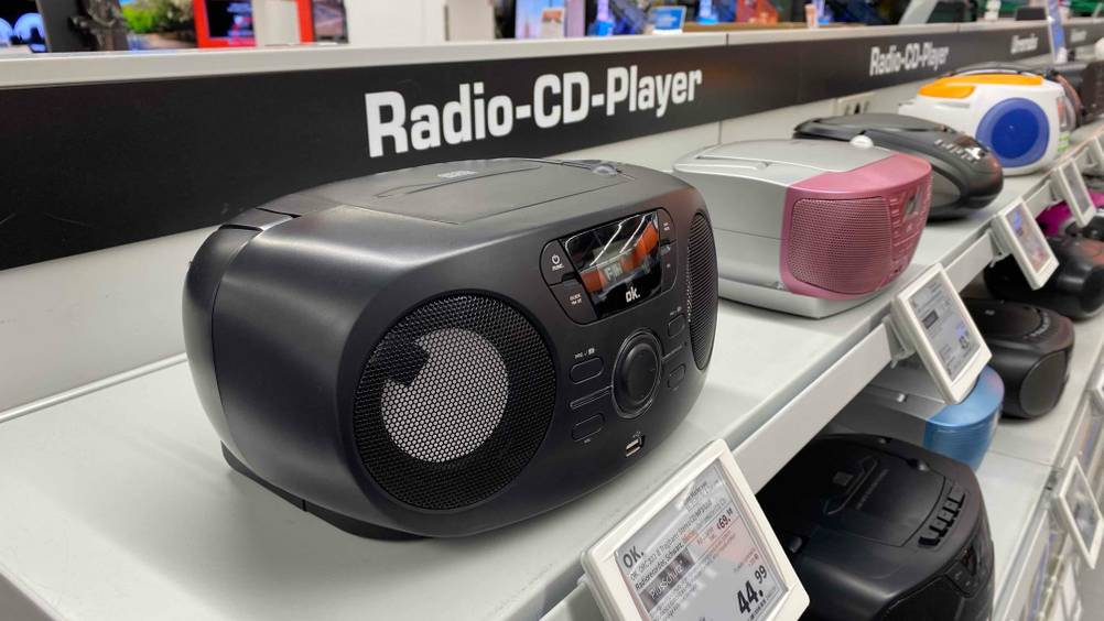 Ein getestetes CD-Radio auf einem Verkaufsregal neben anderen Geräten inklusive Preisschild.