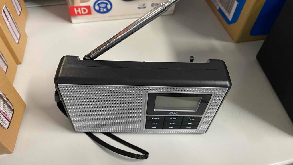 Blick von oben auf ein Taschenradio, das zum Testen mit ausgezogener Antenne auf einer weißen Fläche steht.