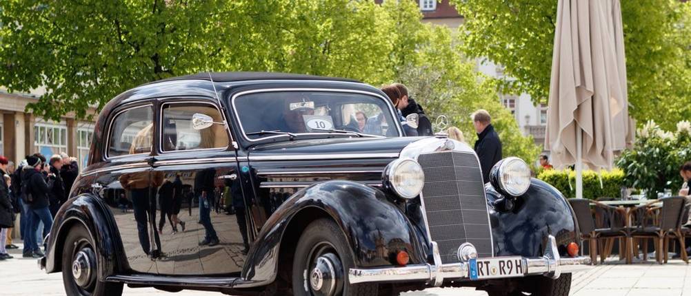 Schwarzer Oldtimer der Marke Mercedes steht auf einem Platz in einer Stadt.