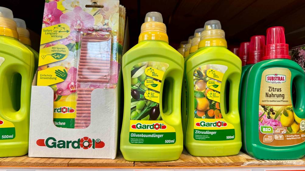 Mehrere Flaschen des getesteten Olivenbaum-Düngers stehen neben anderen Produkten in einem Regal.