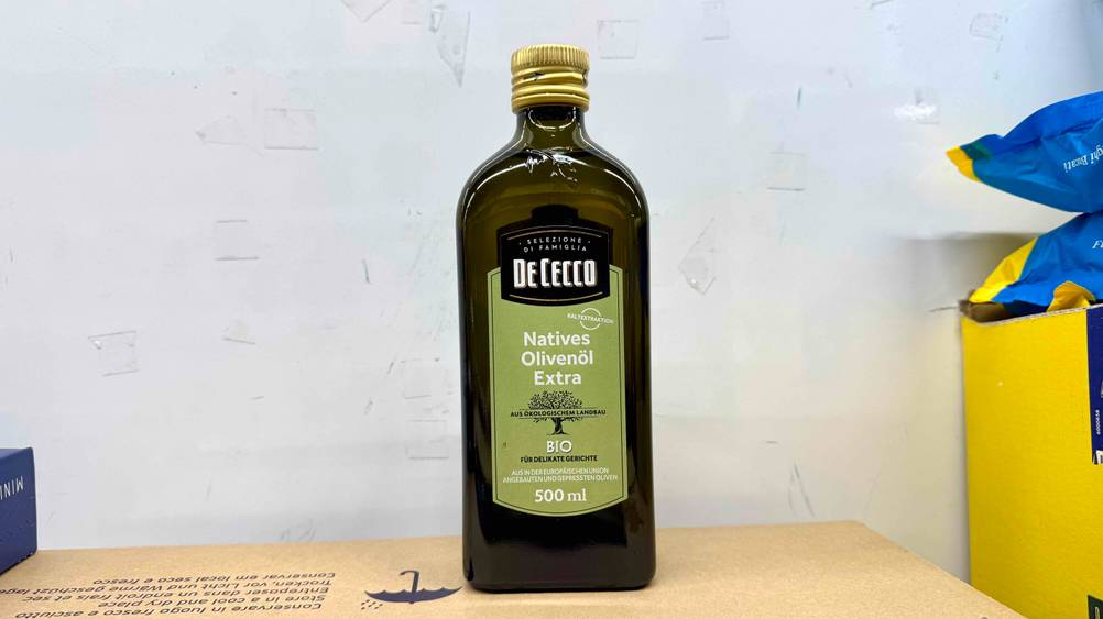 Olivenöl extra vergine im Test: Eine Flasche von vorne vor einer hellen Wand.