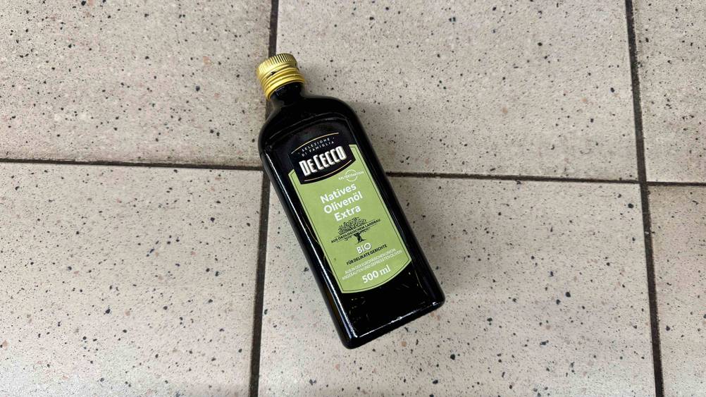 Olivenöl extra vergine getestet: Eine Flasche von oben auf einem Fließenboden liegend.
