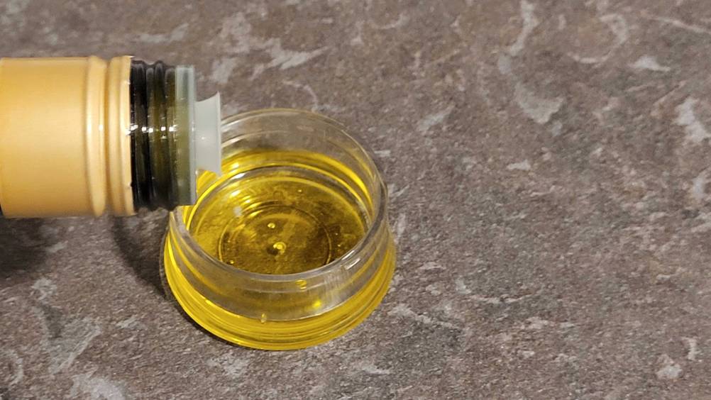 Nahaufnahme der Dosierhilfe einer Flasche Olivenöl im Test, über einer keinen Schale mit Öl.