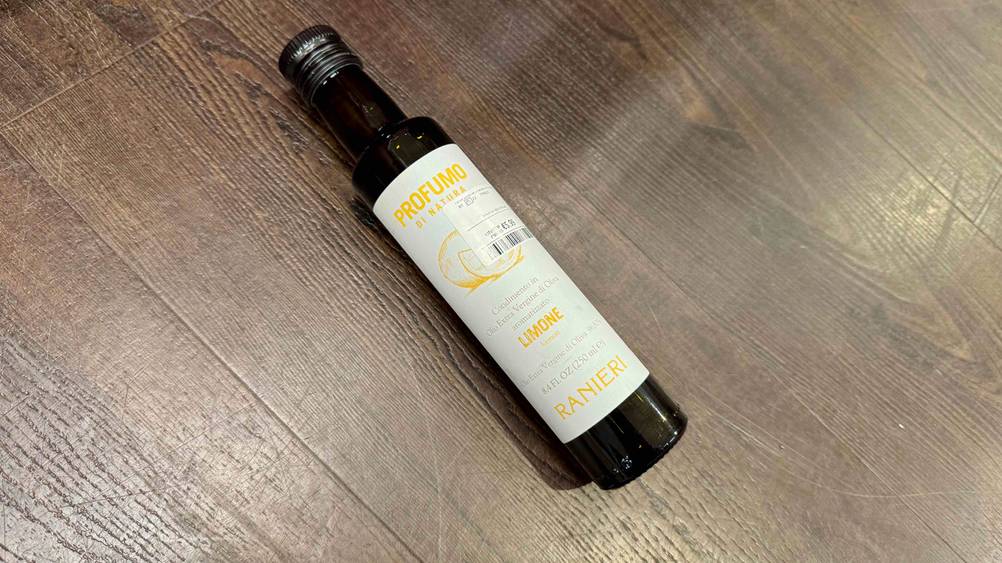 Eine Flasche des getesteten Olivenöl mit Zitrone liegt leicht schräg auf einem Holzboden.