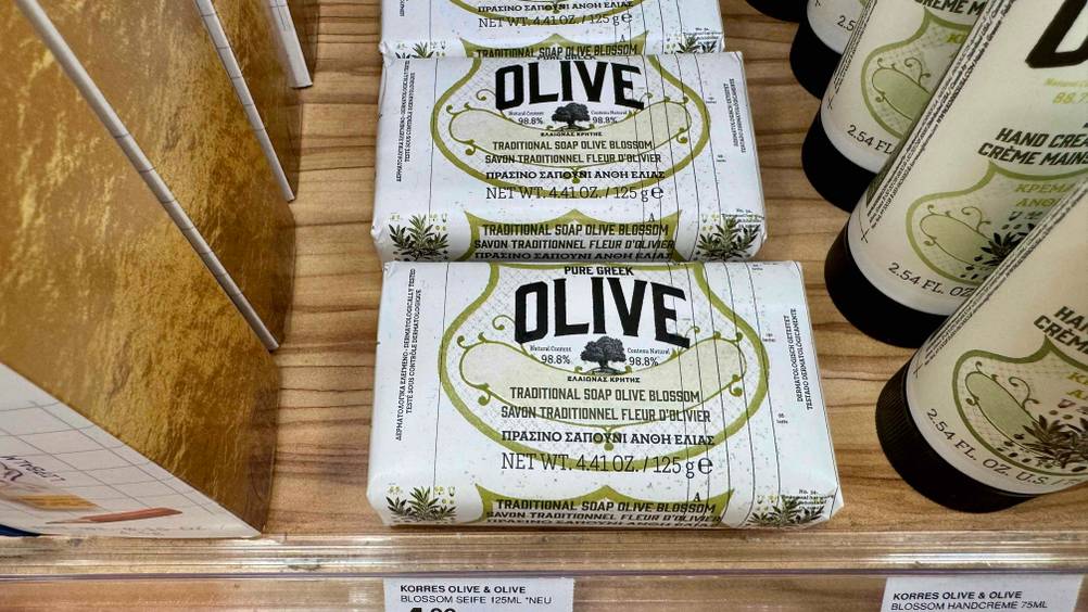 Mehrere verpackte Olivenölseifen im Test neben anderen Produkten auf einem Verkaufsregal.