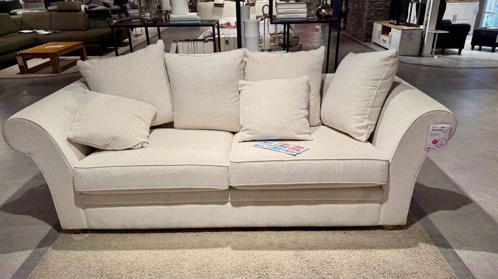 Ansicht von vorn auf ein 3-Sitzer Sofa im Test, das mit einem hellen Stoffbezug und mehreren Kissen ausgestattet ist.