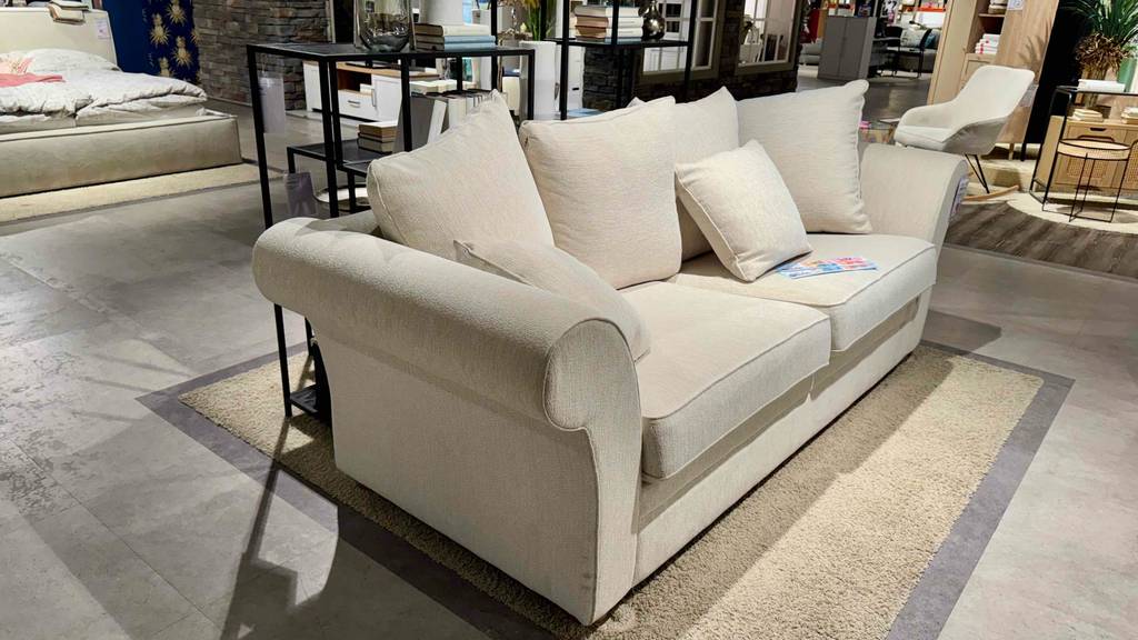 Im Test: Ein 3-Sitzer Sofa mit hellem Stoffbezug, von der Seite betrachtet, steht in einem Möbelgeschäft.
