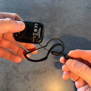 Eine Hand hält eine Halterung an der Schlaufe vom Omron-Schrittzähler fest