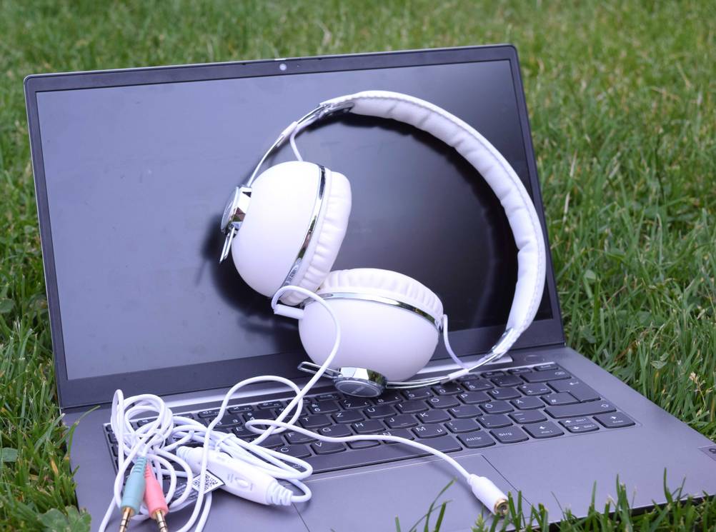 In einer Wiese steht ein Laptop, darauf liegen die getesteten On-Ear-Kopfhörer.