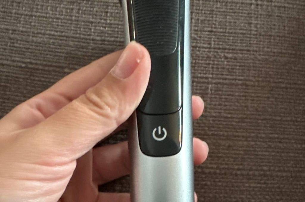 Detailansicht des Griffs eines getesteten Philips One Blade Bartschneiders im schwarz-silbernen Design in einer Hand vor braunem Stoff.