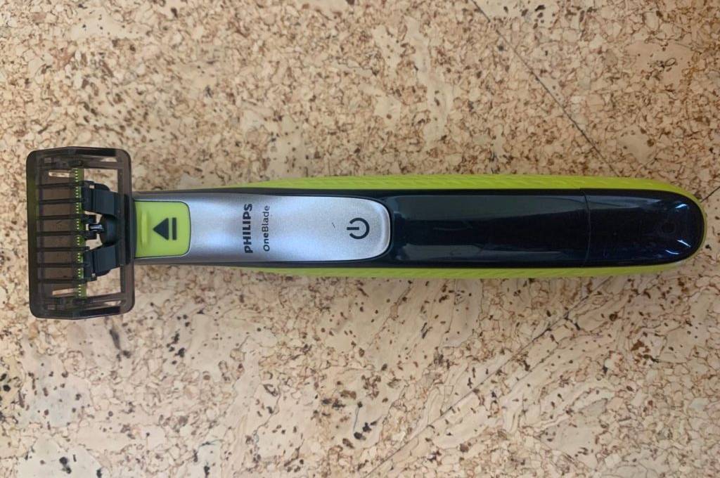 Bartschneider im Test: One Blade Bartschneider von Philips im grün-schwarzen Design liegt mit der Klinge und dem Einschaltknopf nach oben auf einem Kork-Untergrund.