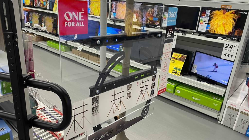 In einem Verkaufsbereich mit einer Vielzahl an ausgestellten Fernsehern befindet sich ein getesteter TV-Ständer für 65 Zoll (1,65 m) der Marke One For All.