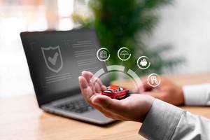 Gebrauchtwagen-kaufen-Test: Eine Person sitzt am Laptop und hält ein rotes Modellauto in der Hand, über dem grafische Darstellungen von Eigenschaften eines Autos schweben.