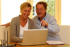 Online-Banking-Software-Test: ein älteres Paar sitzt an einem Tisch und schaut lächelnd auf einen Laptop.