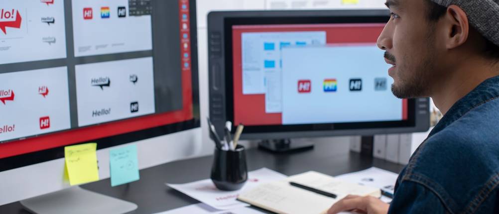 Grafikdesigner arbeitet am Computer neben mehreren Entwurfsskizzen.