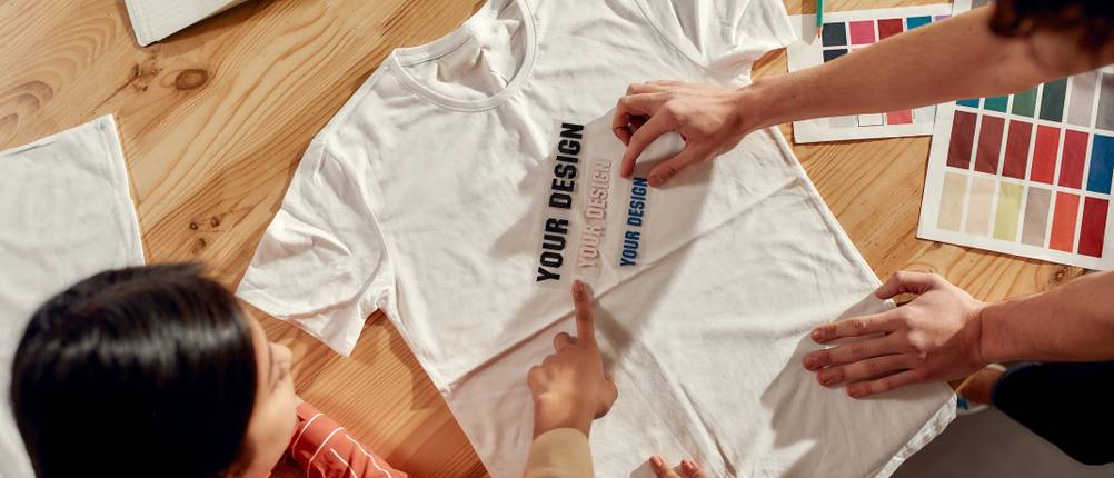 Test der Online-Druckereien: Zwei Personen gestalten zusammen den Aufdruck auf einem weißen T-Shirt.
