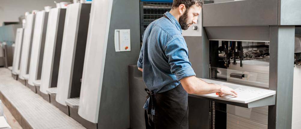 Mitarbeiter arbeitet an einer großen Druckmaschine in einer Druckerei.