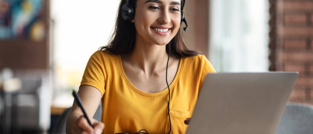 Onlinekurse im Test: Eine Frau nimmt mit einem Headset und Laptop an einem Onlinekurs teil.