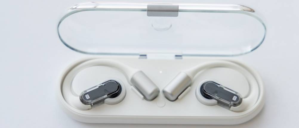 Open-Ear-Kopfhörer mit Bügel getestet und in einem weißen Ladecase vor grauem Hintergrund.