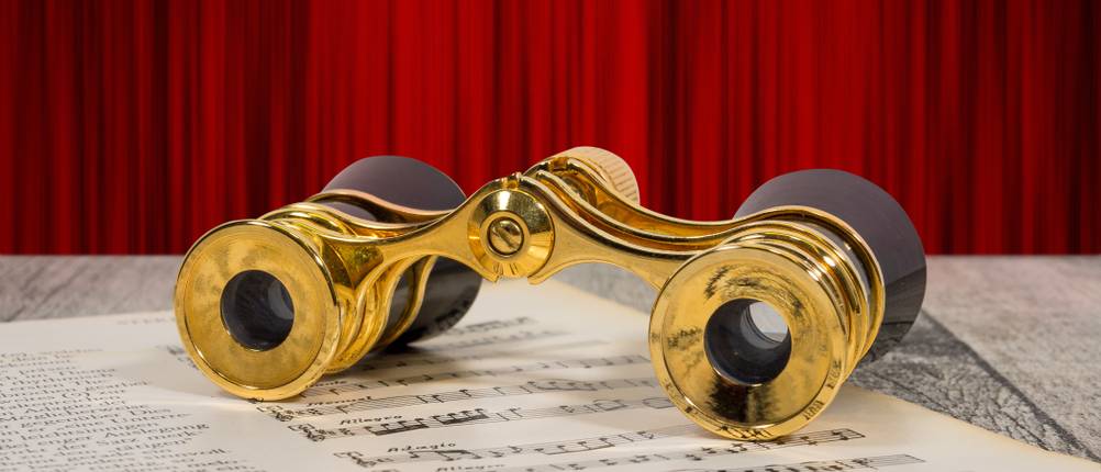 Opernglas-Test: Ein goldenes Opernglas im klassischen Design liegt auf einer Musiknote auf einem Tisch. 
