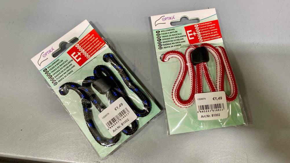 Im Test: Zwei verpackte Brillenbänder liegen auf einer grauen Fläche.