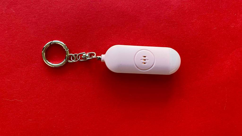 Im Test: Ein Taschenalarm mit Schlüsselring liegt quer auf einer roten Unterfläche.