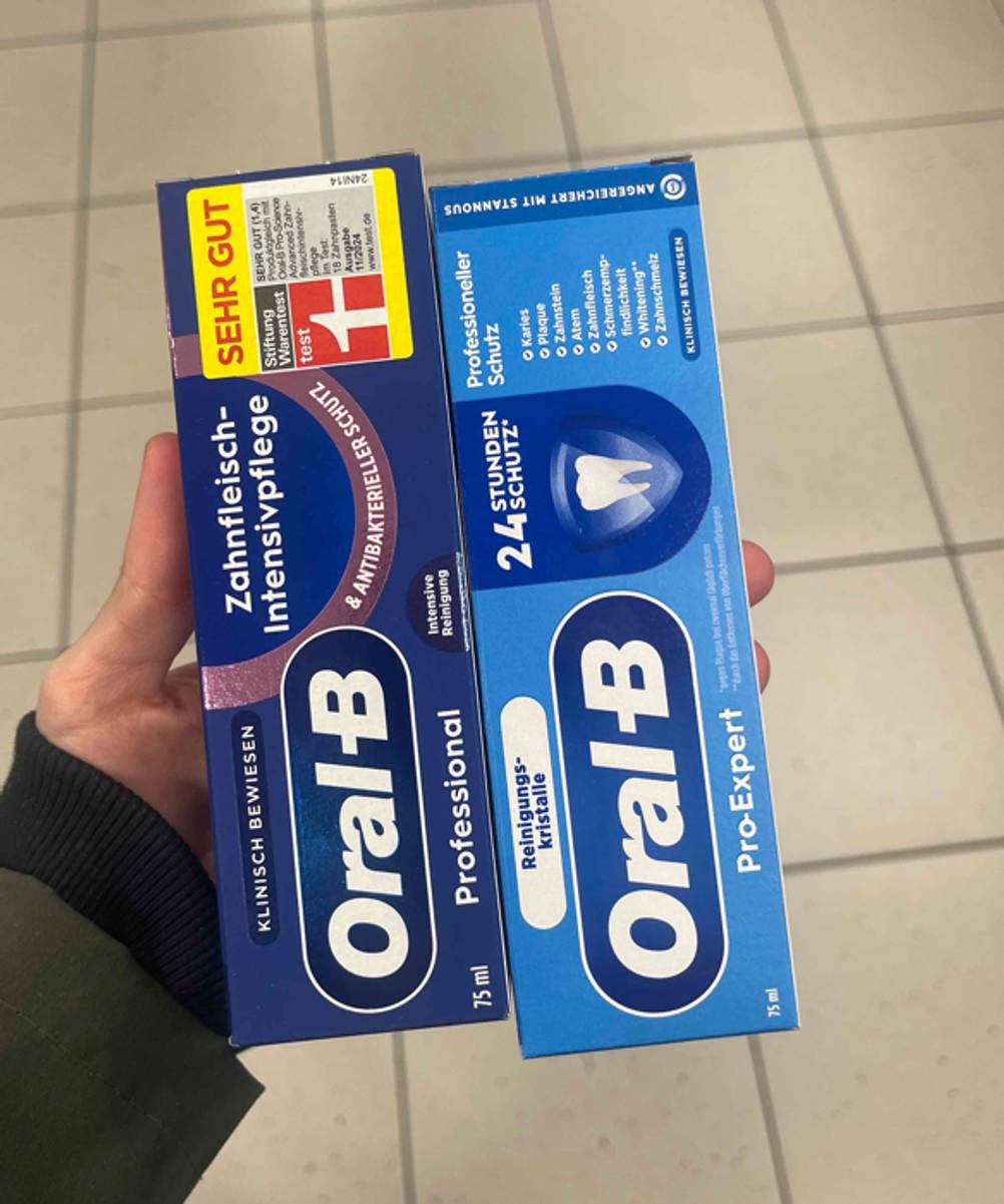 Eine Hand hält zwei Packungen verschiedener Oral-B-Zahnpasta zum testen.