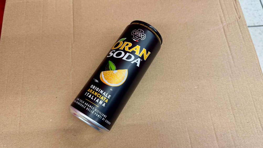 Auf einem Karton liegt eine Dose der Orangenlimonade im Test.