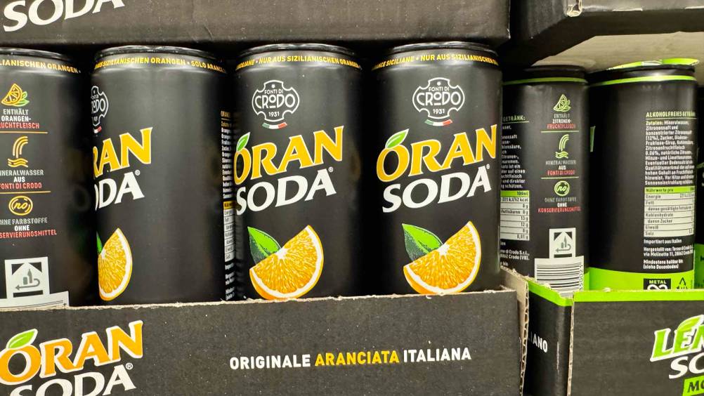 Mehrere Dosen der Orangenlimonade im Test in einem Verkaufsregal.