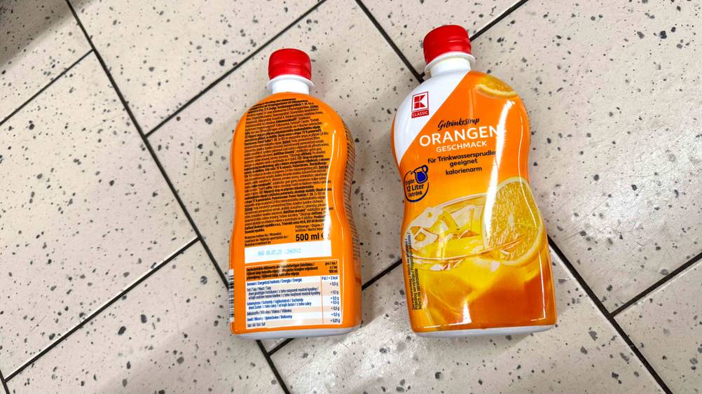 Zwei Flaschen des gestesteten Orangensirups auf einem Boden. Eine von vorne, eine von hinten.