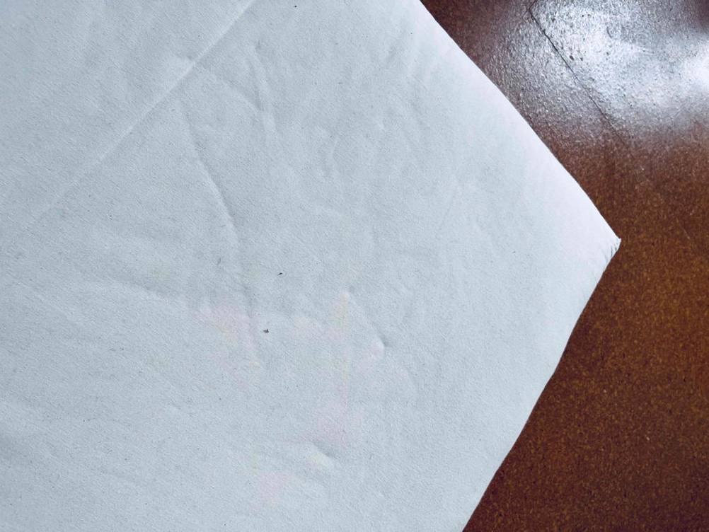 Detailansicht einer Ecke und des Materials einer weißen getesteten Kindermatratze auf braunem Untergrund.