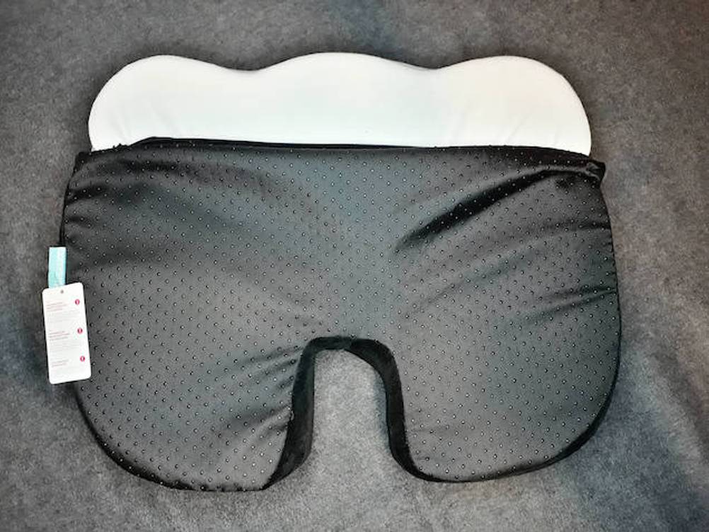Orthopädisches Sitzkissen im Test: Ein orthopädisches Sitzkissen mit halb geöffnetem Bezug liegt auf einer grauen Oberfläche.