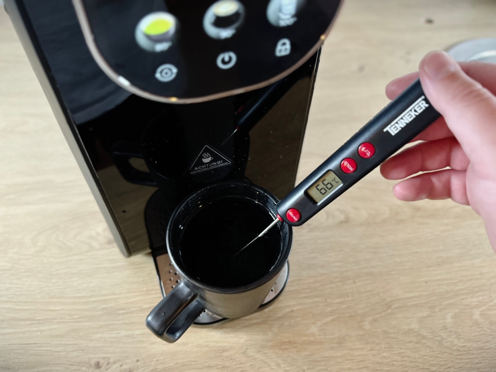 Ein Thermometer misst 66 Grad Celsius in einer schwarzen Tasse unter dem Auslass der Osmofresh Quella Pro Black. Die Temperaturanzeige ist gut sichtbar.